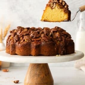 Pecan upside down cake on a cake stand with a cake spatula pulling a piece out of it.
