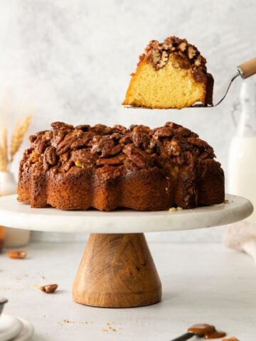 Pecan upside down cake on a cake stand with a cake spatula pulling a piece out of it.