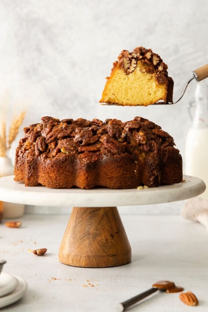 Pecan upside down cake on a cake stand with a cake spatula pulling a piece out of it.