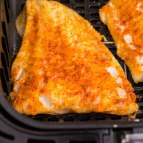 Cooked cod in an air fryer basket.