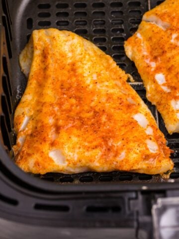 Cooked cod in an air fryer basket.