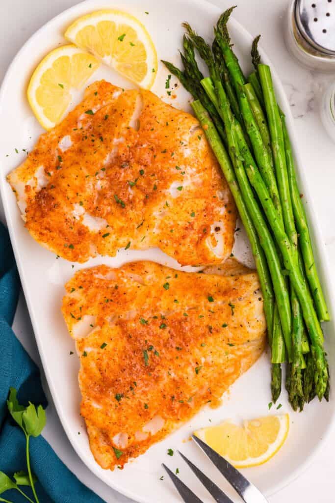 Air fryer cod cooked on a white plate with green beans and lemon.