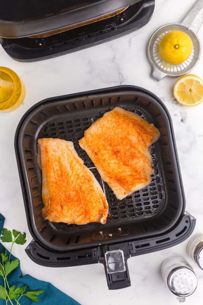 Raw cod in an air fryer basket.