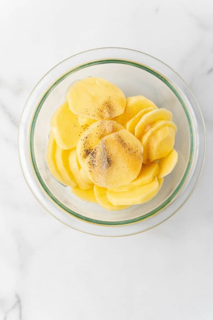 bowl with sliced potatoes and seasonings