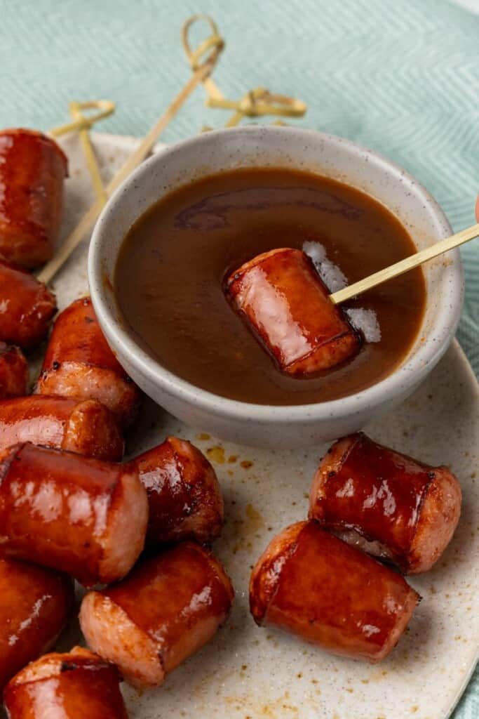 dipping fully cooked smoked sausage into bowl of sauce