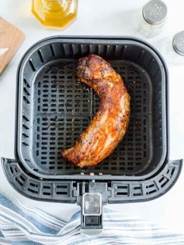 Cooked pork tenderloin in an air fryer basket.