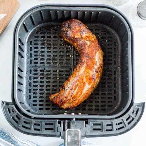 Cooked pork tenderloin in an air fryer basket.
