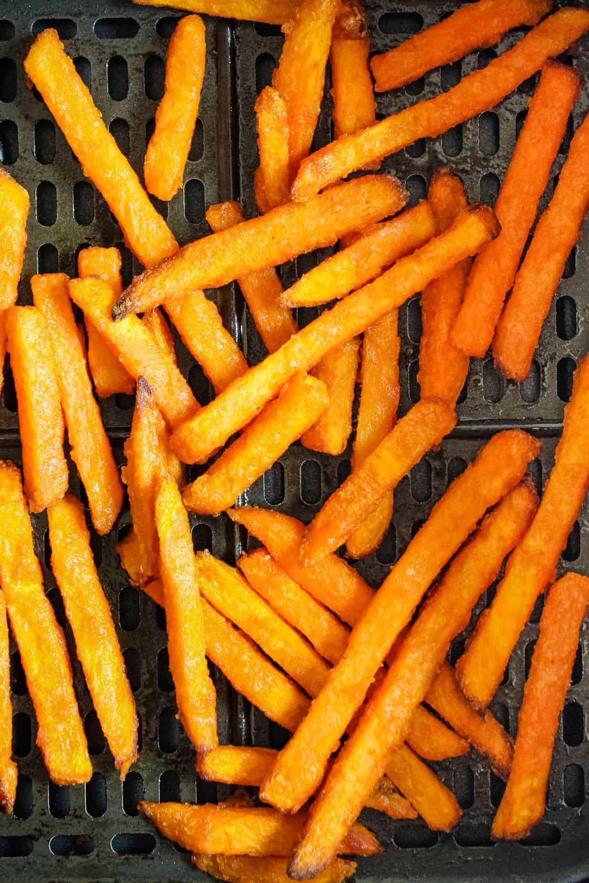 Closeup of frozen sweet potato fries in an air fryer basket.