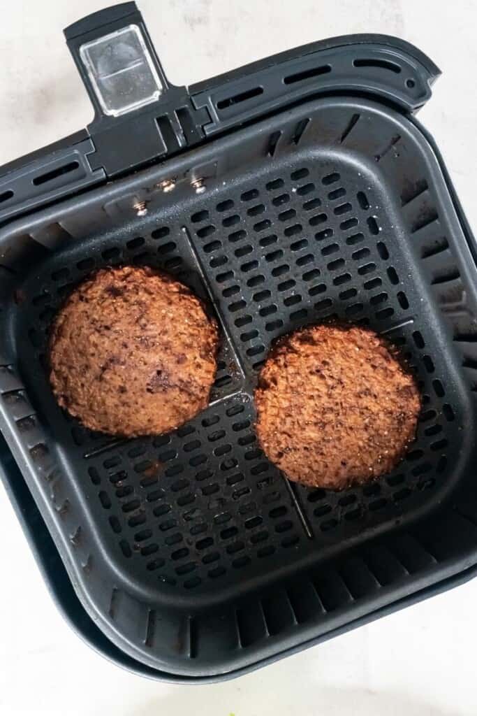 cooked hamburger patties in an air fryer basket