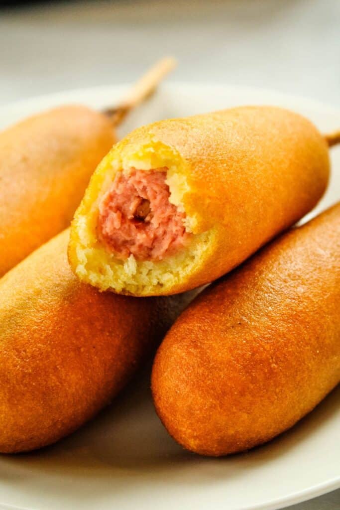 Air fryer corn dogs on a plate with one bitten into.