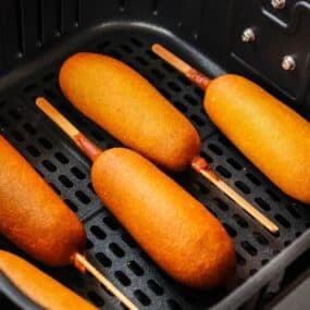 Cooked corn dogs in the air fryer basket.