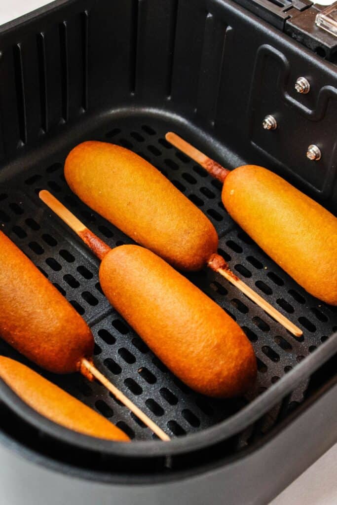 Cooked corn dogs in the air fryer basket.