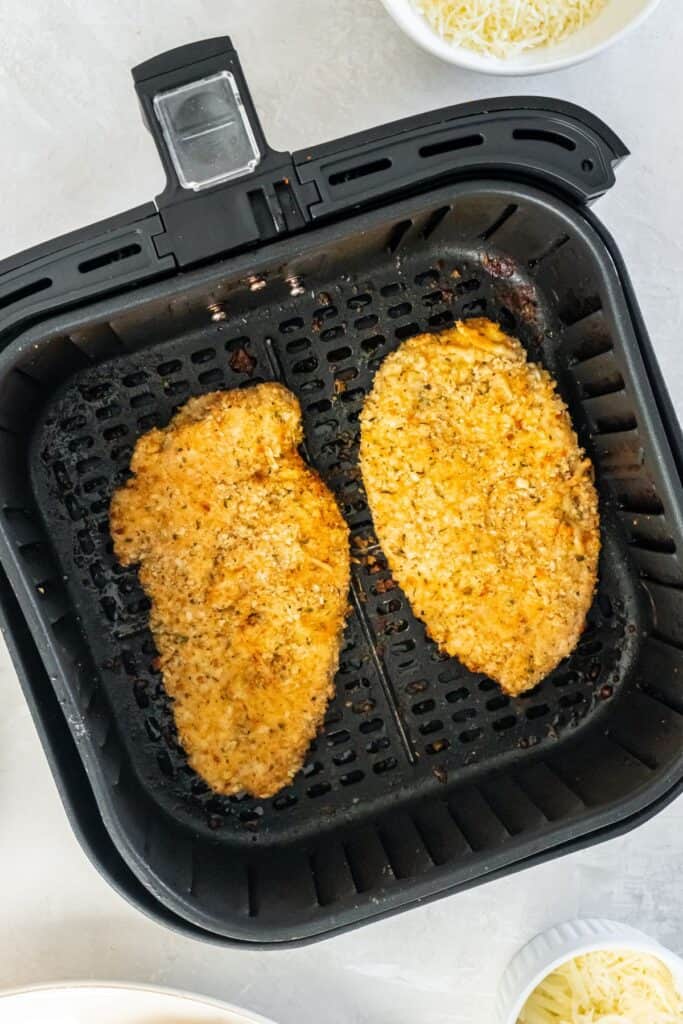 Cooked chicken parm in an air fryer basket about to have sauce and cheese added.