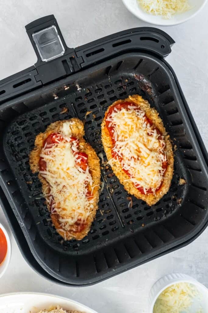 Fully cooked air fryer chicken parmesan in the air fryer basket with cheese melted on top.