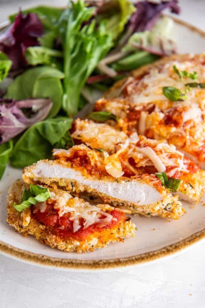Closeup of air fryer chicken parm on a white plate sliced into strips.