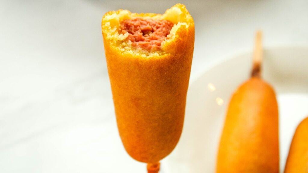 Air fry corn dog being held with a bite out of it.