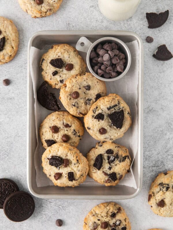 Oreo cheesecake cookies in a small tin storage dish with a side of chocolate chips.