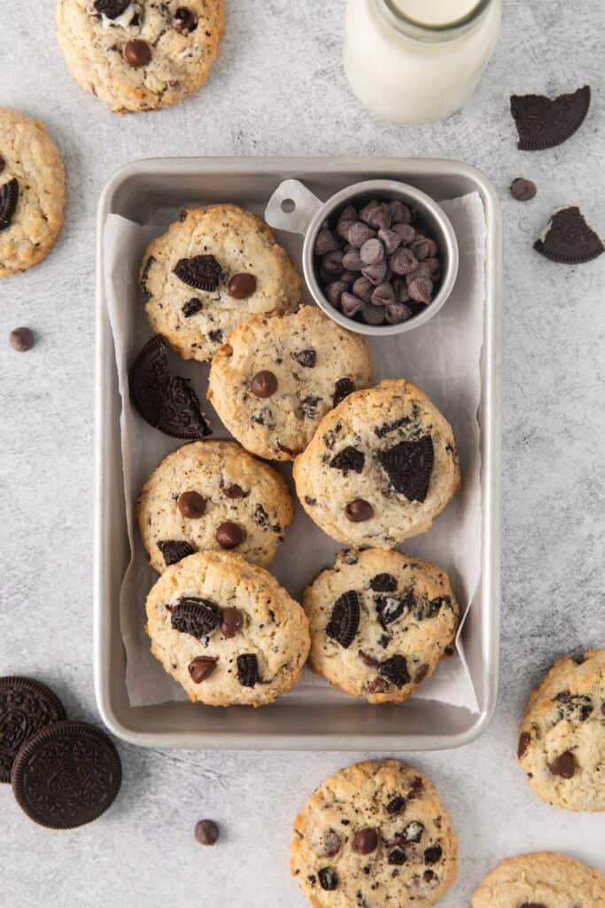 Oreo cheesecake cookies in a small tin storage dish with a side of chocolate chips.