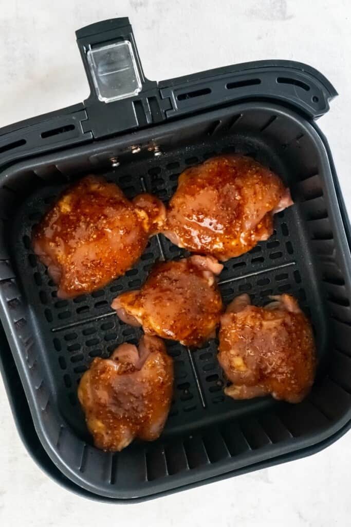 Boneless chicken thighs in a black air fryer basket.