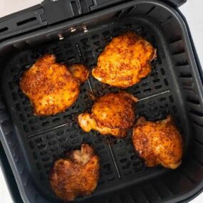 Overhead view of five air fried boneless chicken thighs in a black air fryer basket.