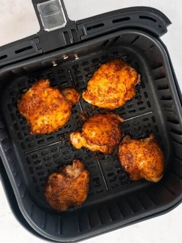 Overhead view of five air fried boneless chicken thighs in a black air fryer basket.