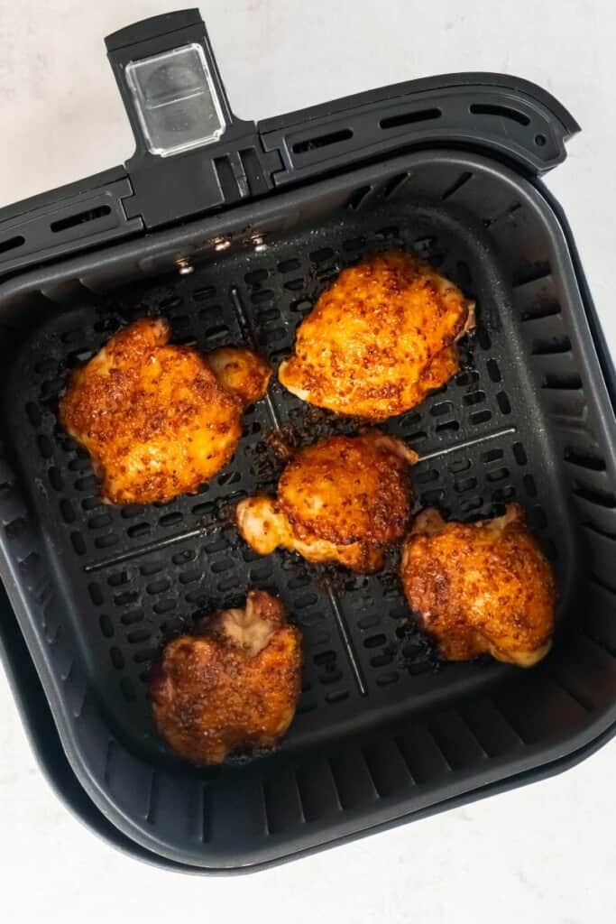 Overhead view of five air fried boneless chicken thighs in a black air fryer basket.