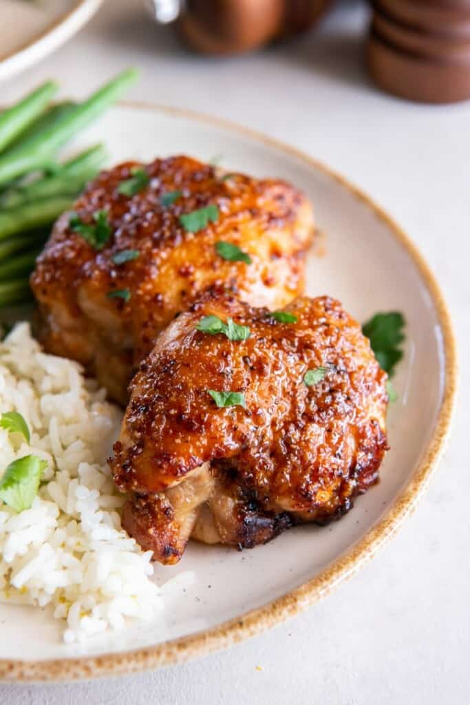 Boneless chicken thighs prepared in the air fryer on a whit plate with rice and green beans