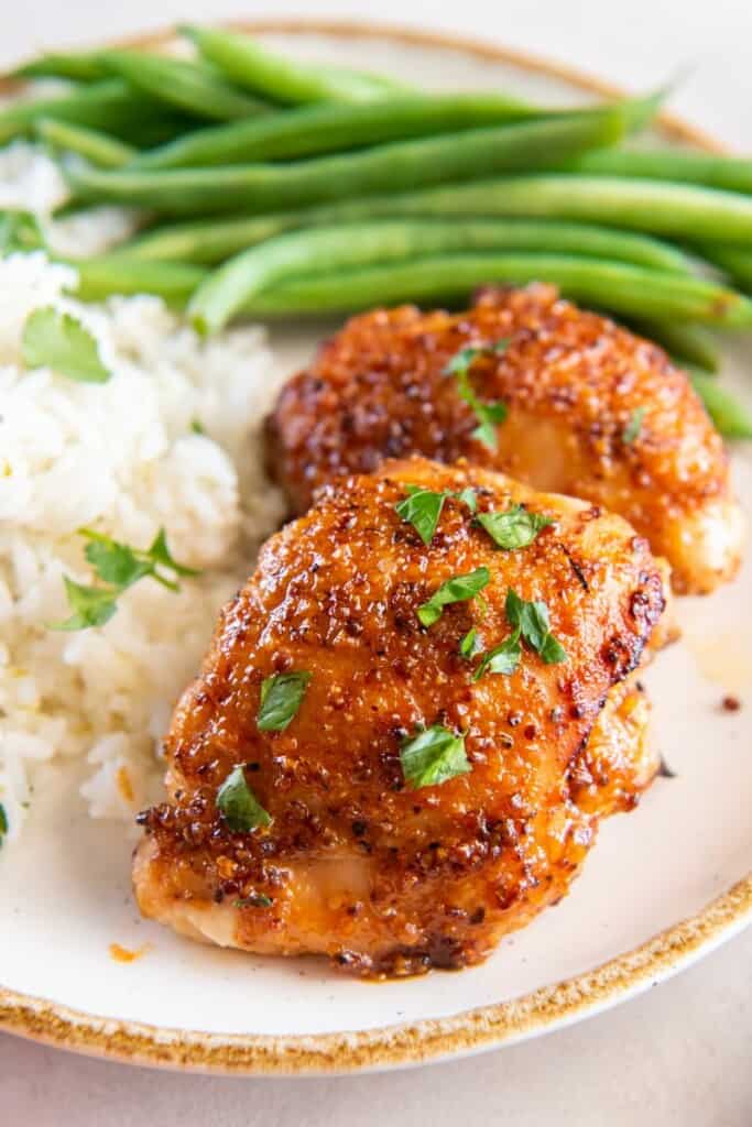 Boneless Chicken Thighs on a white plate with rice and green beans.
