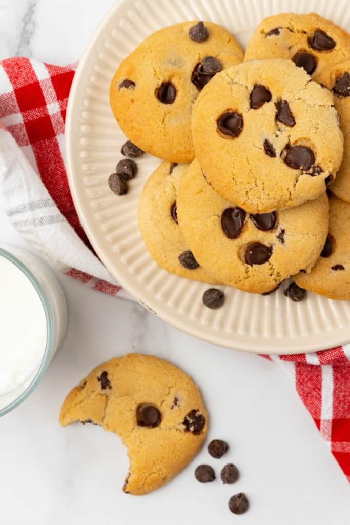 A white plate of air fryer cookies. In the foreground is one cookie with a bite taken out.