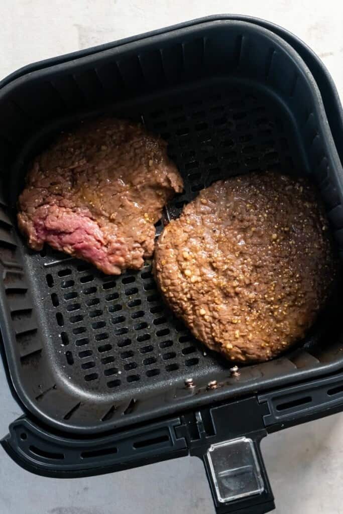 Overhead view of two cube steaks in an air fryer basket.