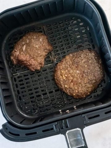 Overhead view of two cube steaks in an air fryer basket.