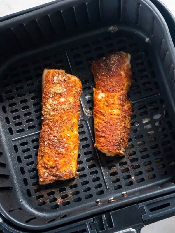 Cooked cod in a black air fryer basket.