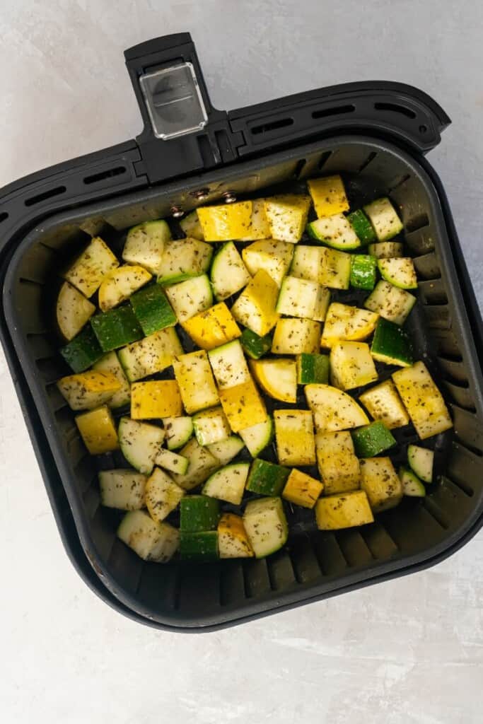 Overhead view of squash and zucchini in a black air fryer basket.