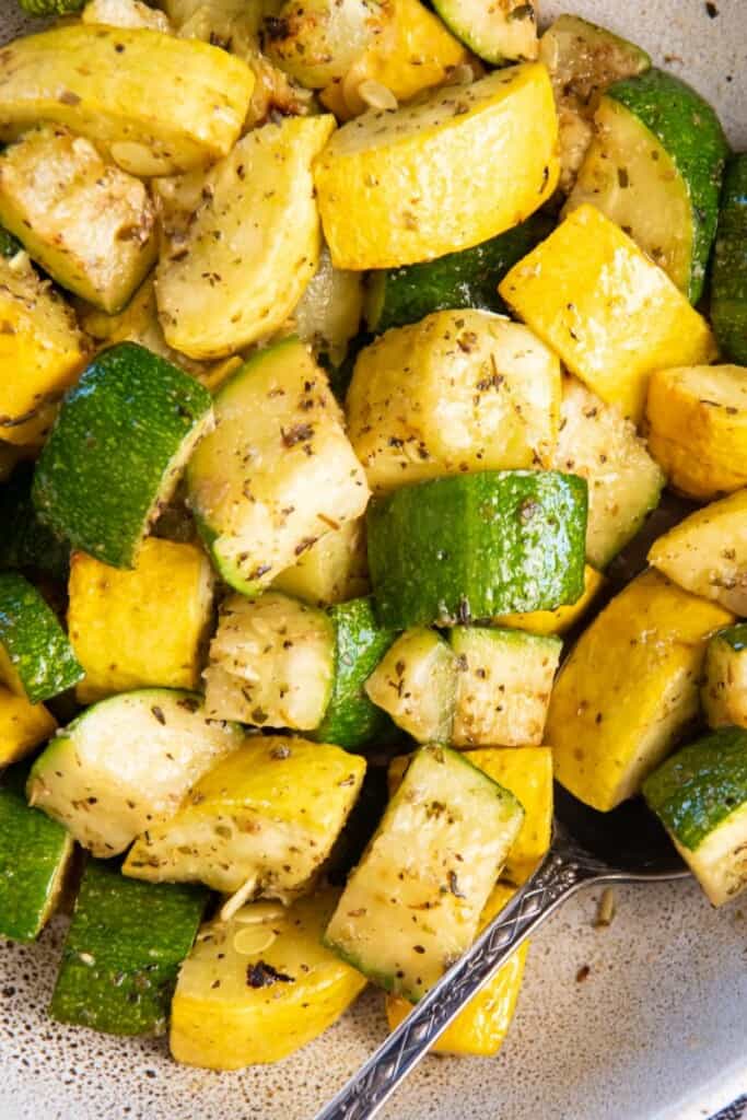 Closeup view of air fried squash and zucchini in a white bowl with a spoon.