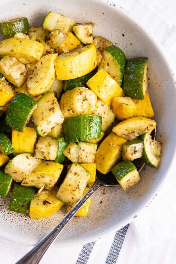 Overhead view of squash and zucchini in a white bowl with a spoon.