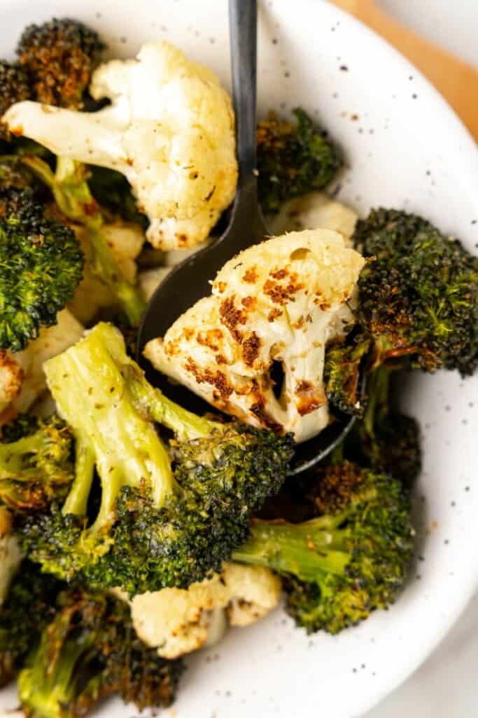 Closeup view of air fried broccoli and cauliflower in a white bowl.