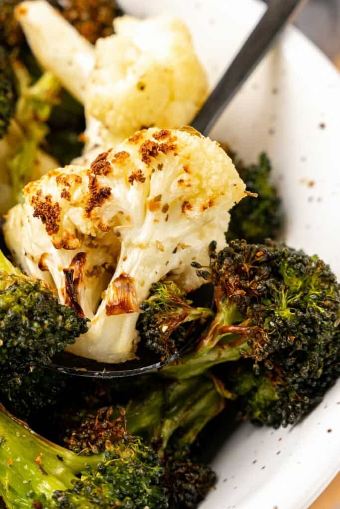 Closeup of air fried broccoli and cauliflower in a white bowl.