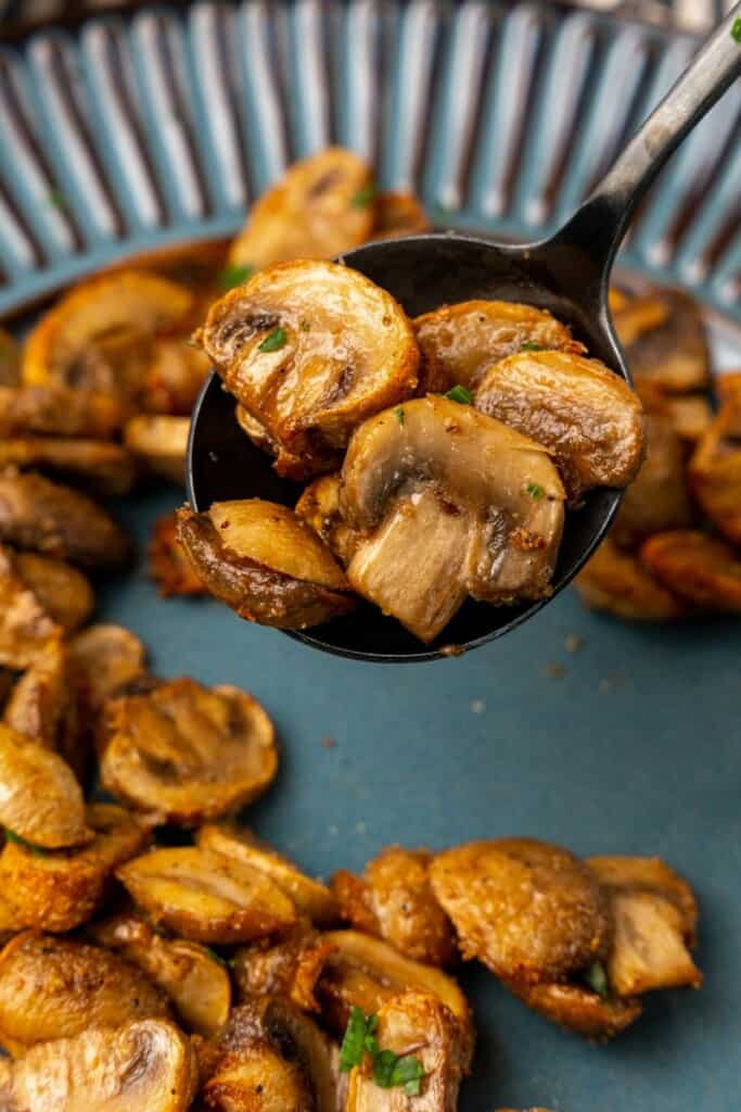 Closeup view of air fried mushrooms on a blue plate. A silver spoon is holding a raised bite of mushrooms.