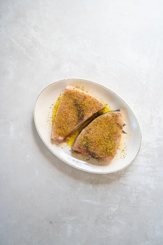 Swordfish coated in seasonings on a white plate.