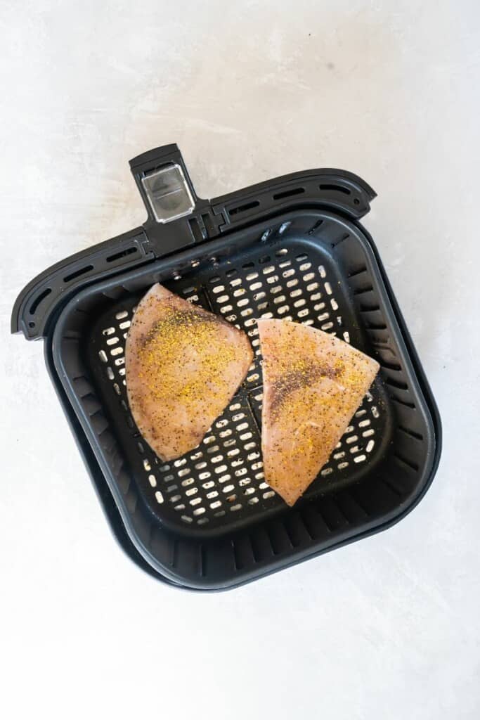 Two seasoned swordfish steaks lying in a black air fryer basket.