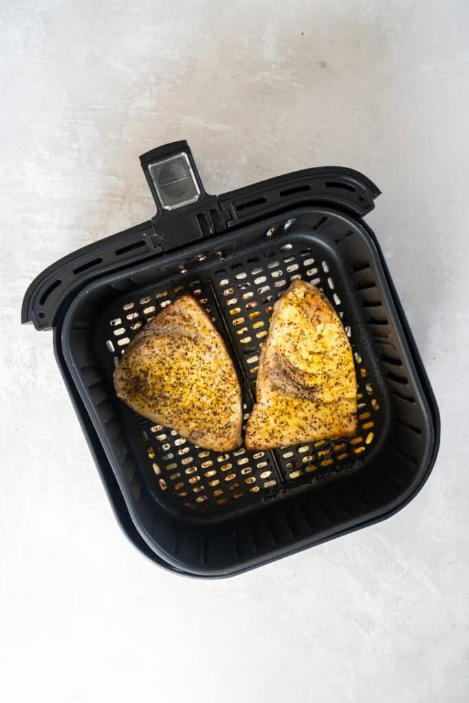 Two air fried swordfish steaks resting in a black air fryer basket.