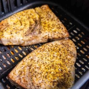 Closeup of two air fried swordfish steaks in a black air fryer basket.