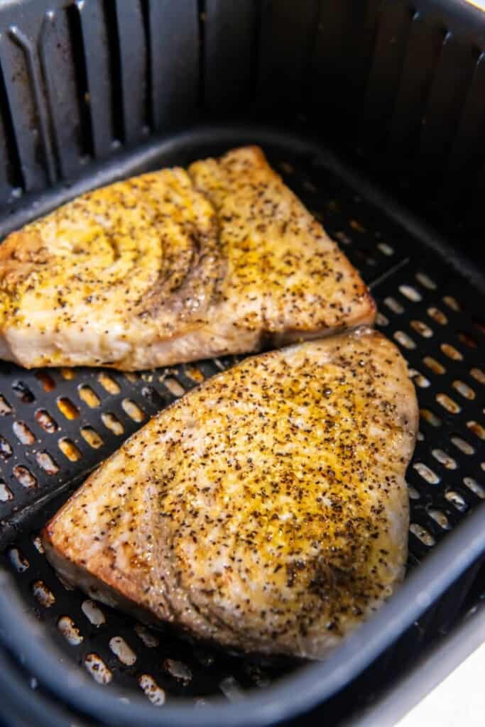 Closeup of two air fried swordfish steaks in a black air fryer basket.