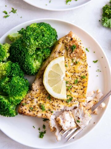 Air Fryer Swordfish on a white plate topped with lemon, served with broccoli.