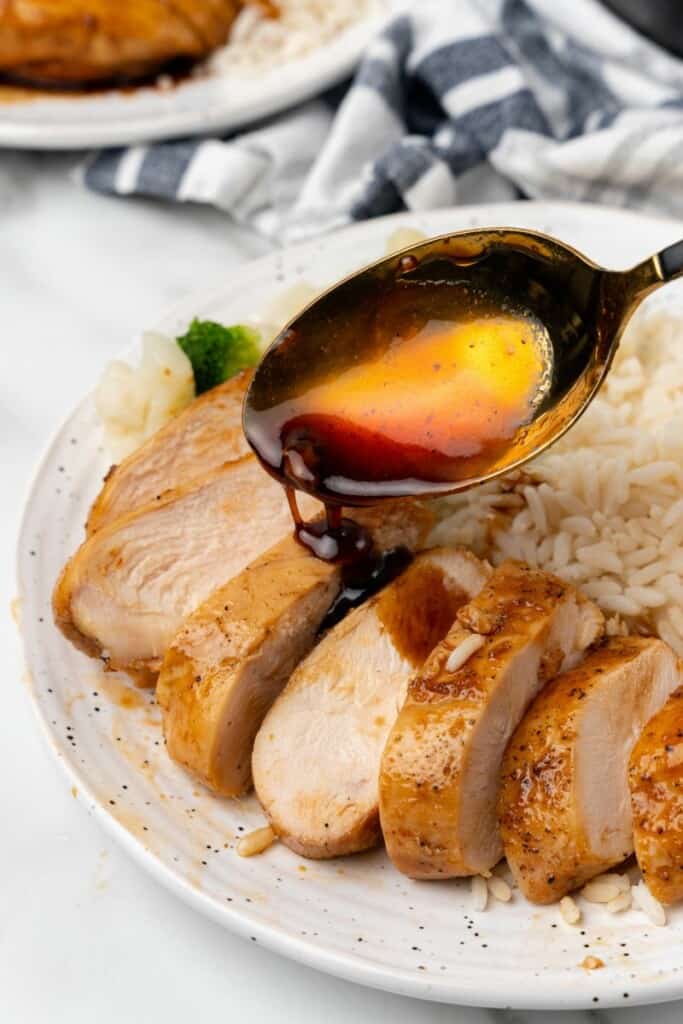 Pouring sauce over sliced chicken breast on a white plate.
