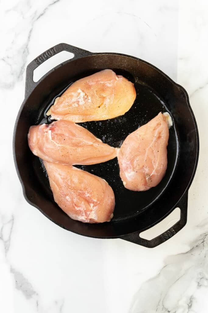 Overhead view of chicken breasts cooking in a cast iron skillet.