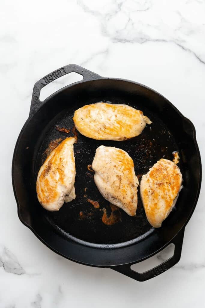 Overhead view of chicken breasts cooking in a cast iron skillet.