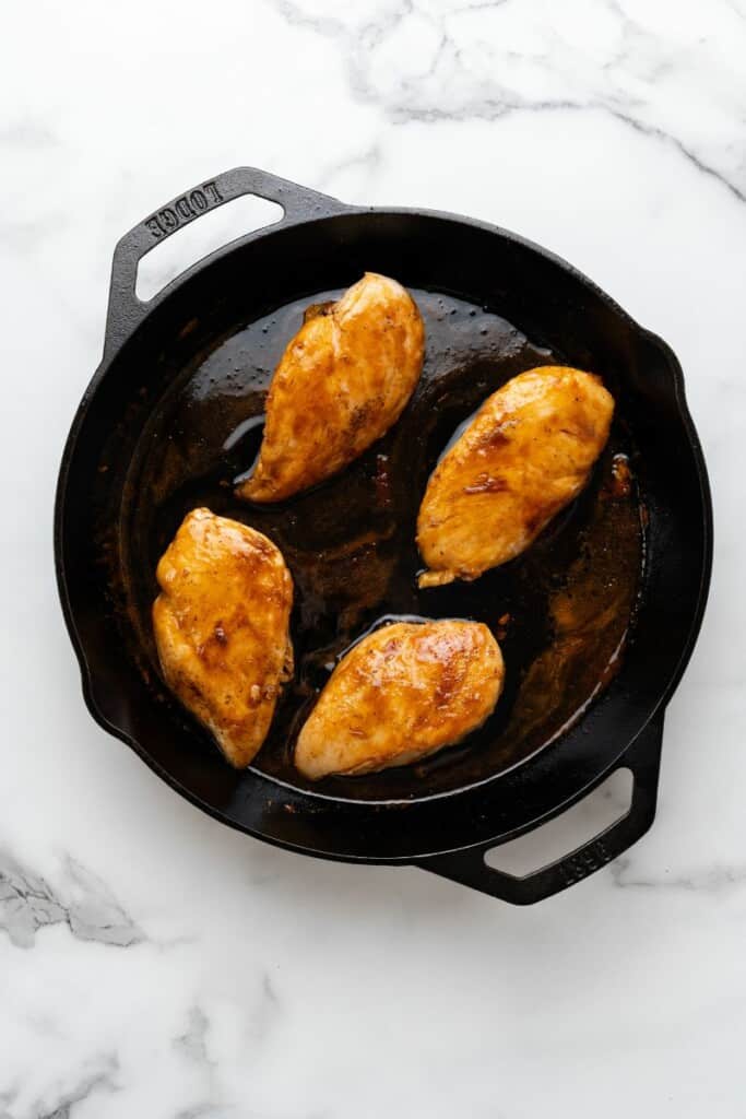 Overhead view of chicken breasts that have cooked in a cast iron skillet.