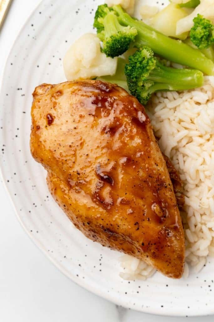 Overhead view of a chicken breast with rice and broccoli on a white plate.
