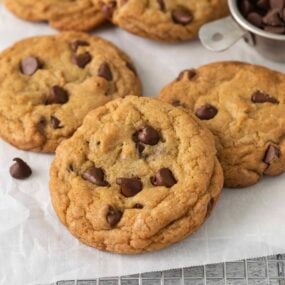 Baked Chocolate Chip Cookies resting on a cooling rack lined with parchment paper.